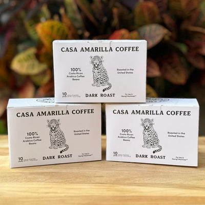 Three boxes of Casa Amarilla Coffee Jaguar Blend pods on a wooden surface with tropical foliage in the background