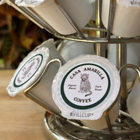 Casa Amarilla Coffee Jaguar Blend pods in a metal carousel on a wooden surface with tropical foliage in the background