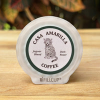 Casa Amarilla Coffee Jaguar Blend pod on a wooden surface with tropical foliage in the background
