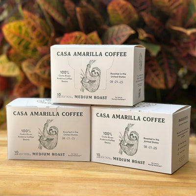 Three boxes of Casa Amarilla Coffee Sloth Blend pods on a wooden surface with tropical foliage in the background