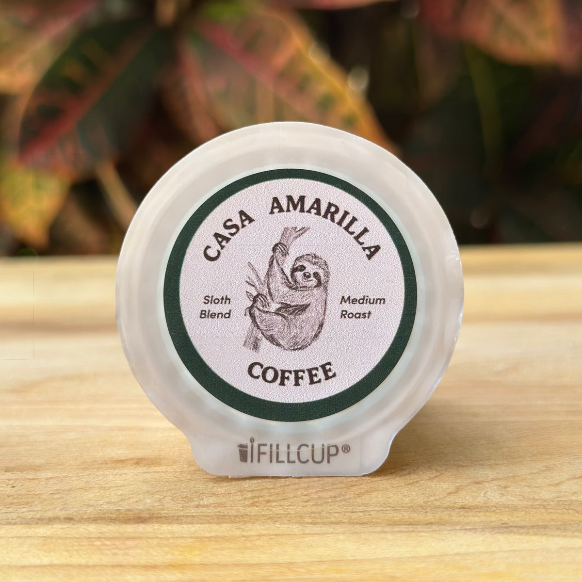 Casa Amarilla Coffee Sloth Blend pod on a wooden surface with tropical foliage in the background