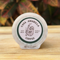 Casa Amarilla Coffee Sloth Blend pod on a wooden surface with tropical foliage in the background